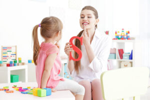 a little girl working with a speech therapist who is holding up a letter "S"