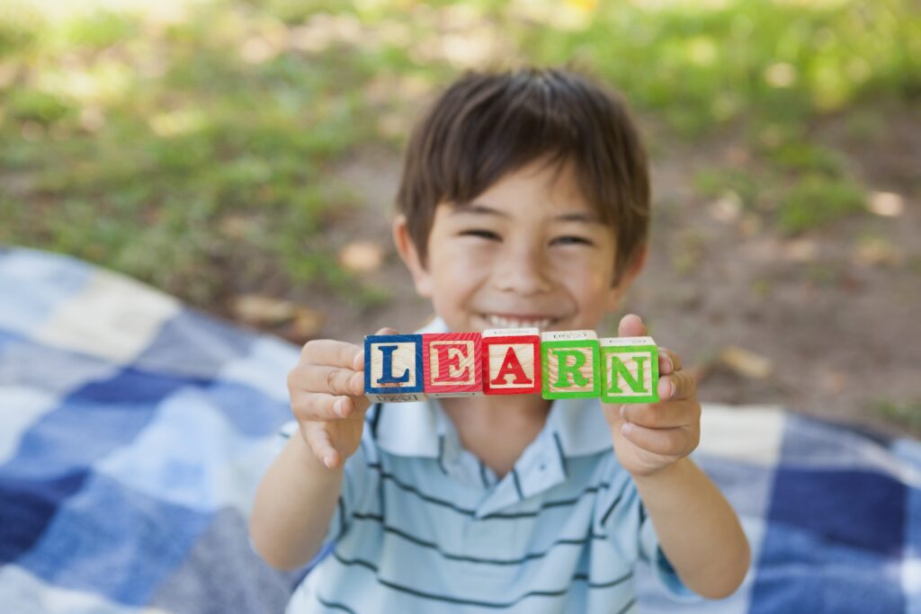 happy boy holding block alphabets as 'learn' at park
