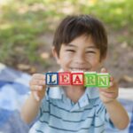 happy boy holding block alphabets as 'learn' at park