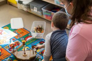 A member of our staff working closely with a young child on a play mat, with toys and crayons